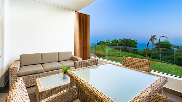 A modern outdoor seating area with a glass-top table and wicker furniture, overlooking a lush landscape and the sea. - Modern Studio l Ocean Views l Steam Room (Cape Town)