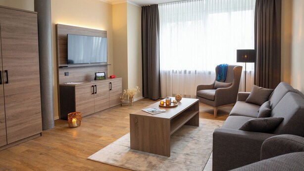 Una sala de estar moderna con un sofá, una mesa de centro, un televisor montado en la pared y un ventanal con cortinas.