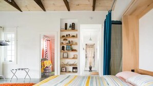 Un dormitorio con cama, techo de madera, repisas con adornos y una ventana.