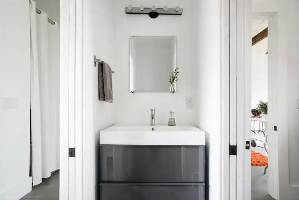 Een moderne badkamer met een witte wastafel, donkere kastjes, een spiegel en een handdoekrek.