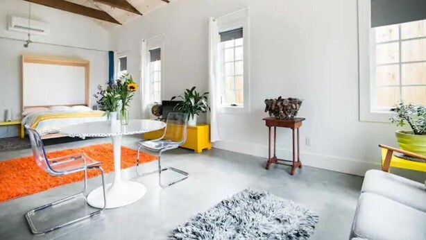 Una habitación moderna con una cama, una mesa redonda con sillas, una pequeña mesita de madera y un ventanal grande.