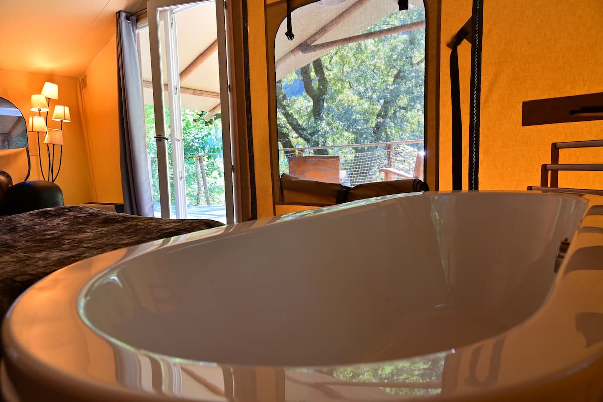 A modern bathroom with a large bathtub, a window with a view of trees, and a wooden bench.