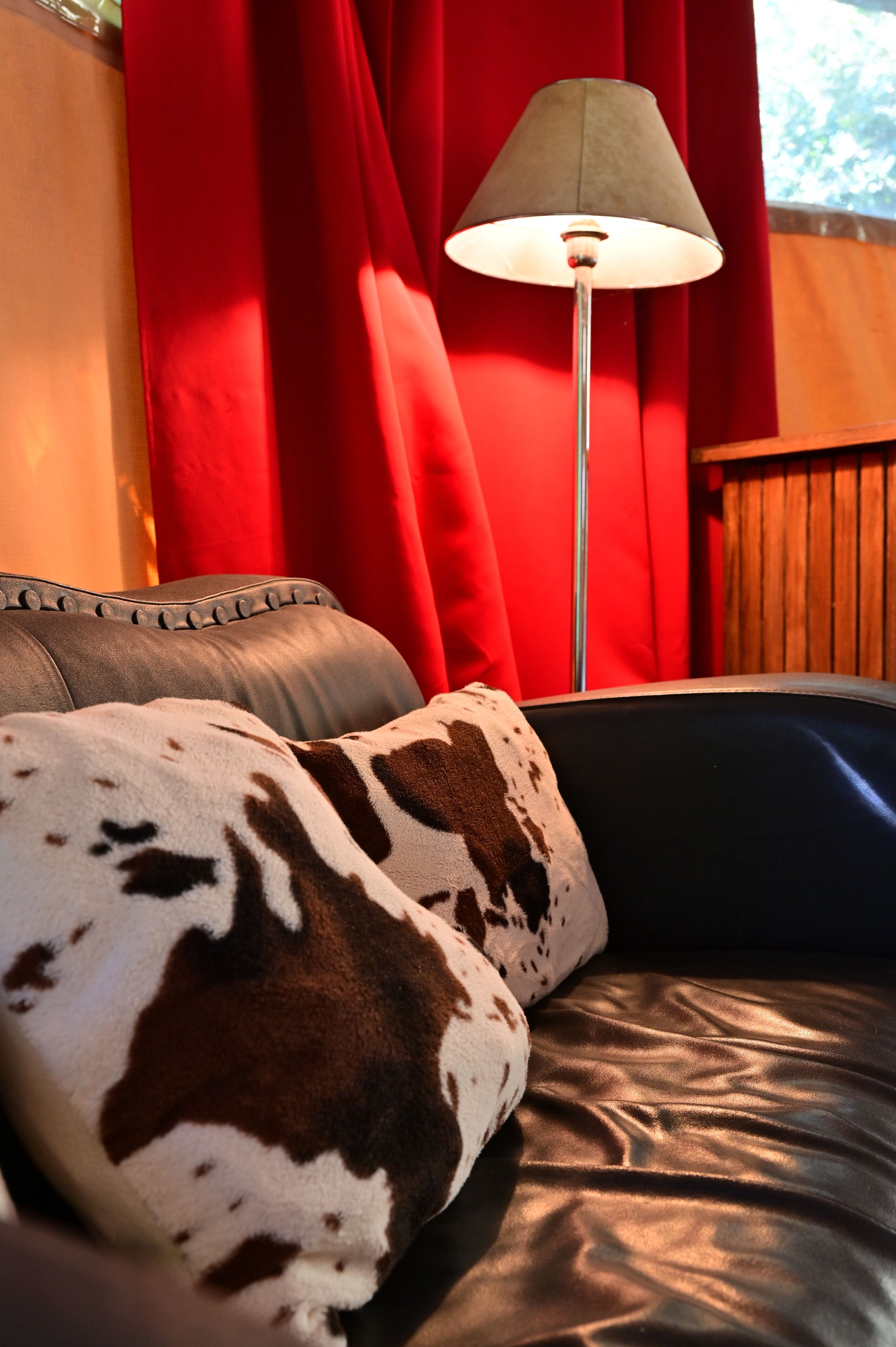 Een leren bank met een kussen van runderleer, een vloerlamp en rode gordijnen.