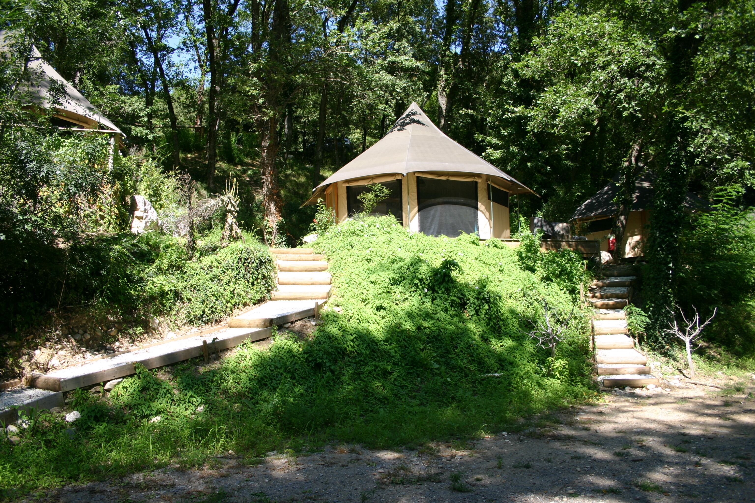A rustic wooden structure with a conical roof, surrounded by dense greenery and a stone staircase leading up.