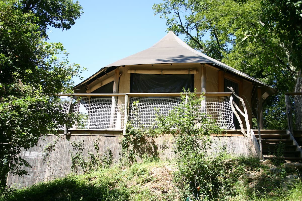 A wooden cabin with a sloped roof, surrounded by trees and a wooden fence.
