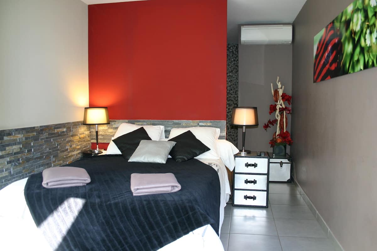 A modern bedroom with a large bed, two bedside tables, a red accent wall, and a decorative plant.