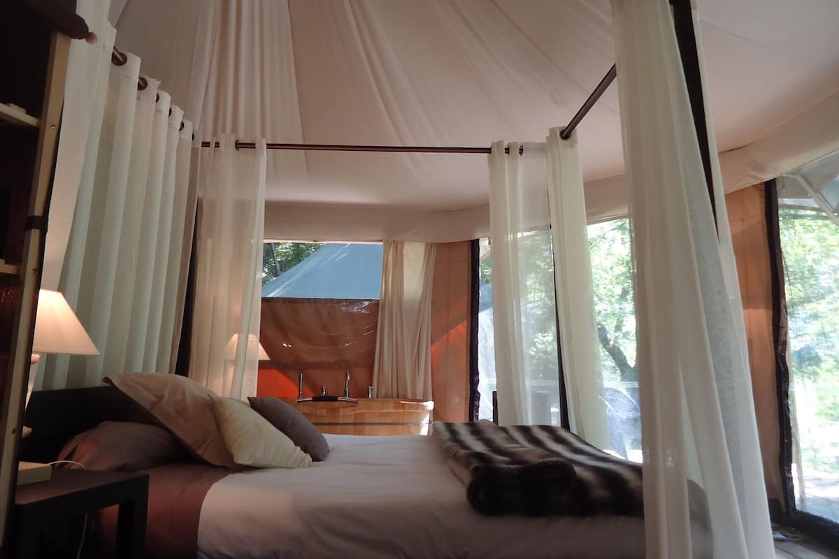A bedroom with a canopy bed, a bedside table, and a view of the outdoors.