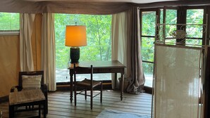 A room with a wooden floor, a table with a lamp, a chair, a sofa, and a view of greenery outside. - Prehistoric Lodge (Vallon-Pont-d'Arc)