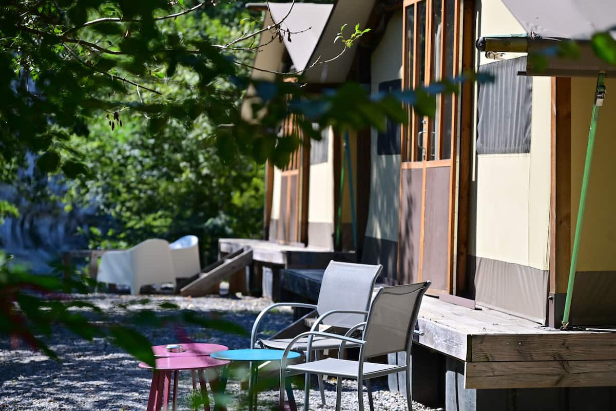 A wooden deck with outdoor seating, including chairs and tables, surrounded by trees.