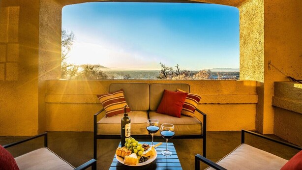 A cozy seating area with a sofa and two chairs, a table with a bottle, glasses, and a fruit platter, and a large window offering a scenic view. - Extraordinary Capitol Hill Home! (Salt Lake City)