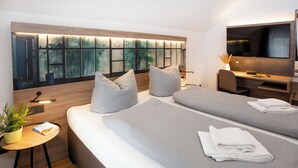 Une chambre d’hôtel moderne avec deux lits, un bureau, une télévision et une grande fenêtre donnant sur la ville.