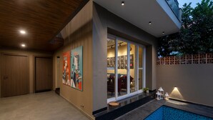 Una casa moderna con piscina, puertas de madera y un amplio ventanal que da a una sala de estar.