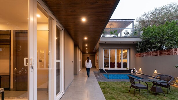 Una casa moderna con un corredor cubierto, una piscina y mobiliario de exterior.