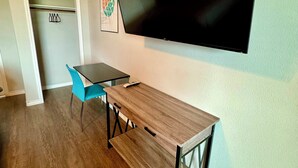 A room with a wooden table, a blue chair, a flat-screen TV mounted on the wall, and a door with a coat rack. - The 409 Bolivar Beach Hotel (Port Bolivar)