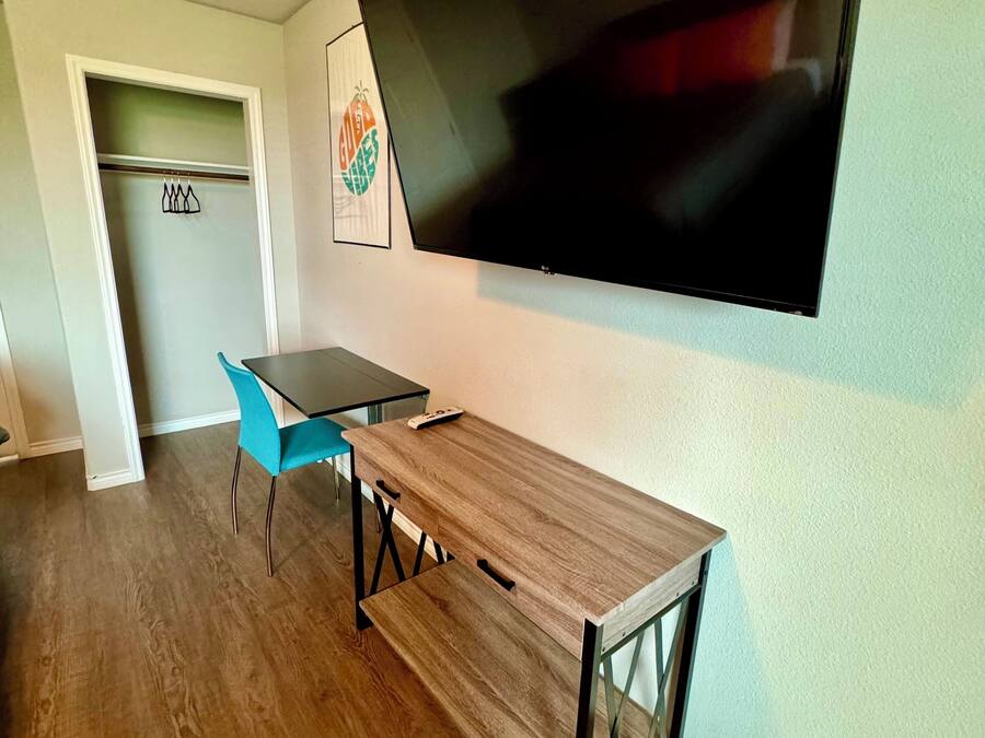 A room with a wooden table, a blue chair, a flat-screen TV mounted on the wall, and a door with a coat rack.