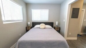 A bedroom with a bed, two bedside tables, and two windows with blinds. - Coastal Breezes -Walk to the Beach (Lantana)