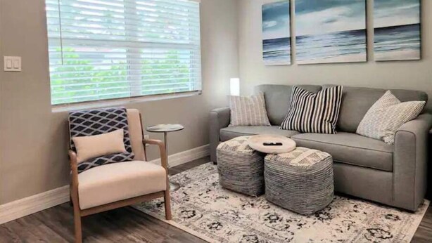 Una sala de estar con un sofá gris, un sillón estampado y una pequeña mesa redonda. Hay tres obras de arte colgadas en la pared que representan paisajes marinos.