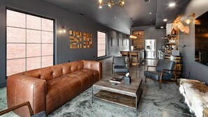A modern living room with a leather sofa, a coffee table, and a fireplace. There is a kitchen area in the background with a dining table and chairs.