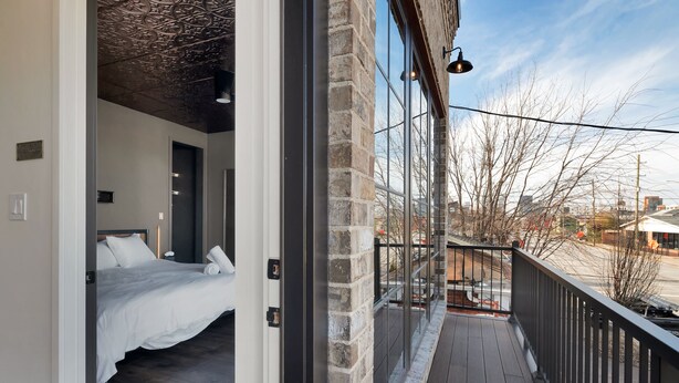 A bedroom with a bed, a wooden floor, a stone wall, and a balcony with a railing.