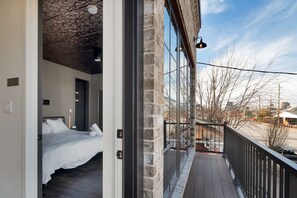 A bedroom with a bed, a wooden floor, a stone wall, and a balcony with a railing. - The Cooperage ~ NULU ~ 4 Bedroom/3 Baths (Louisville)