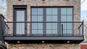 A two-story building with a brick facade, large windows, and a balcony with metal railings.