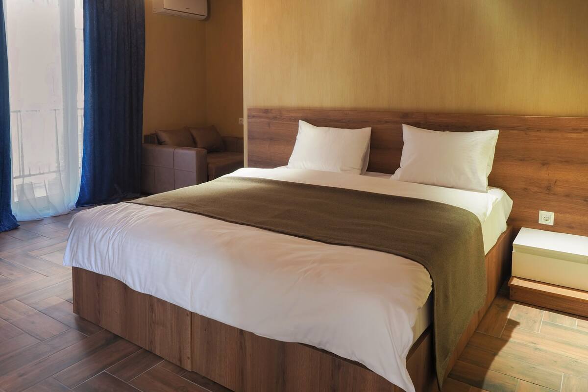 A neatly made bed with a wooden headboard, a bedside table, and a chair in a hotel room.