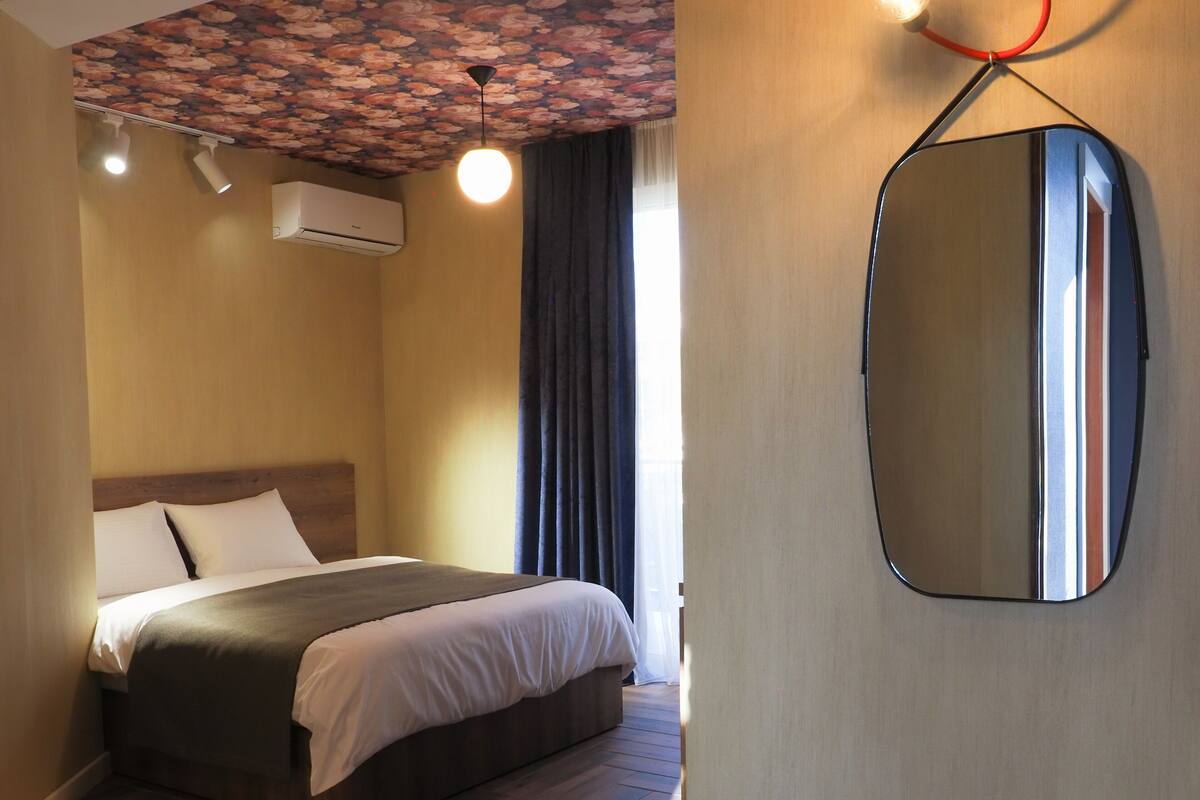 A hotel room with a bed, a large mirror, and an air conditioning unit on the wall.