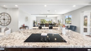 A modern kitchen with a central island, a dining area with a large window, and a living area with a blue sofa. - Oasis Overlook, Have Fun in Pool/Hot Tub/Putt Grn (Phoenix)