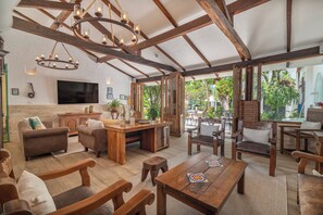 A spacious living area with wooden furniture, a large TV, and a ceiling with exposed beams.