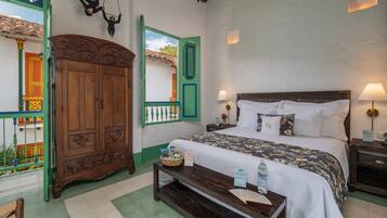 A bedroom with a bed, bedside tables, a wooden wardrobe, and a window with a view of a colorful building.