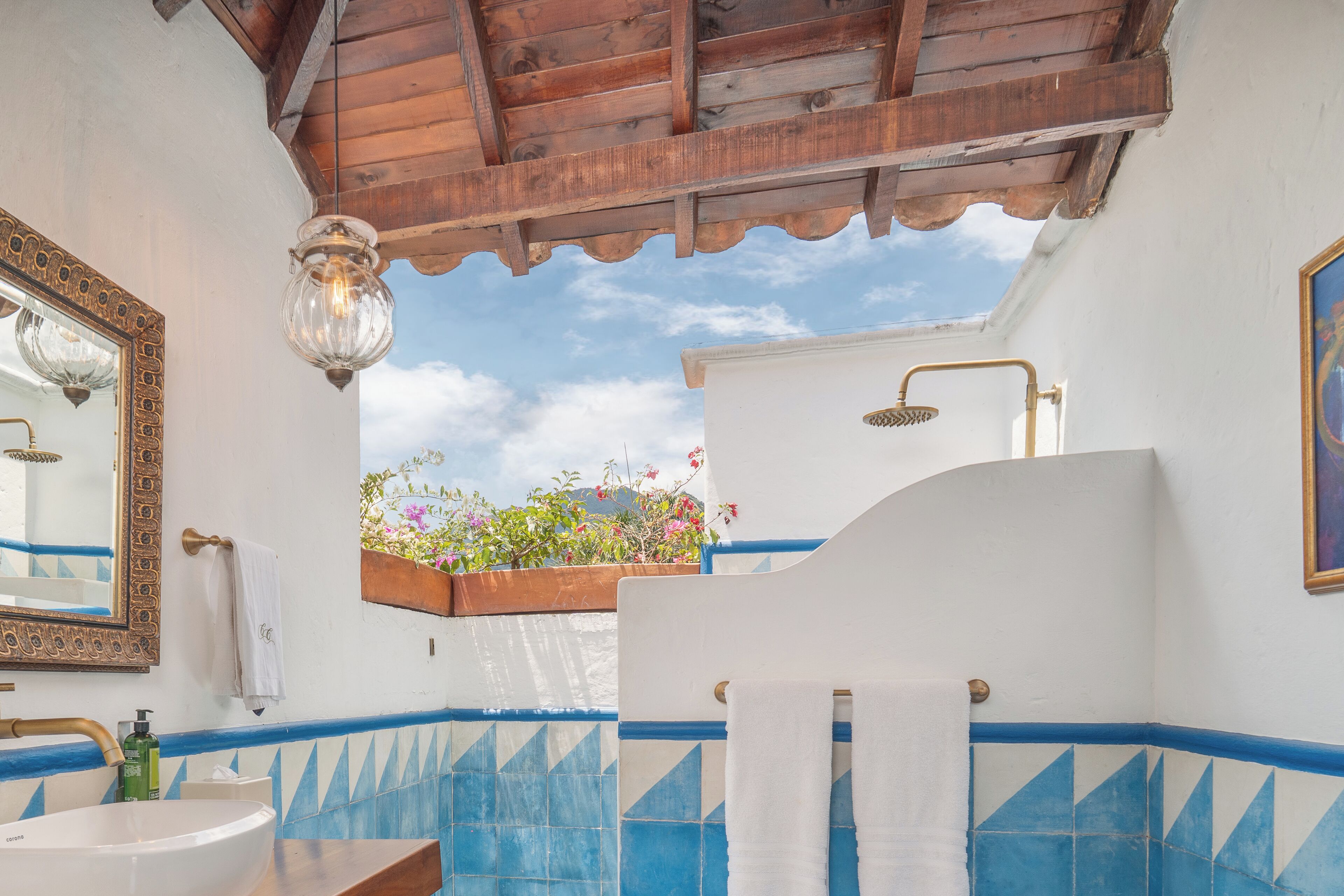 Un baño con un lavabo blanco, paredes con azulejos azules, techo de madera y ducha con grifo dorado.