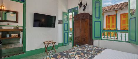 A bedroom with a bed, a TV, a wooden wardrobe, and a green door.