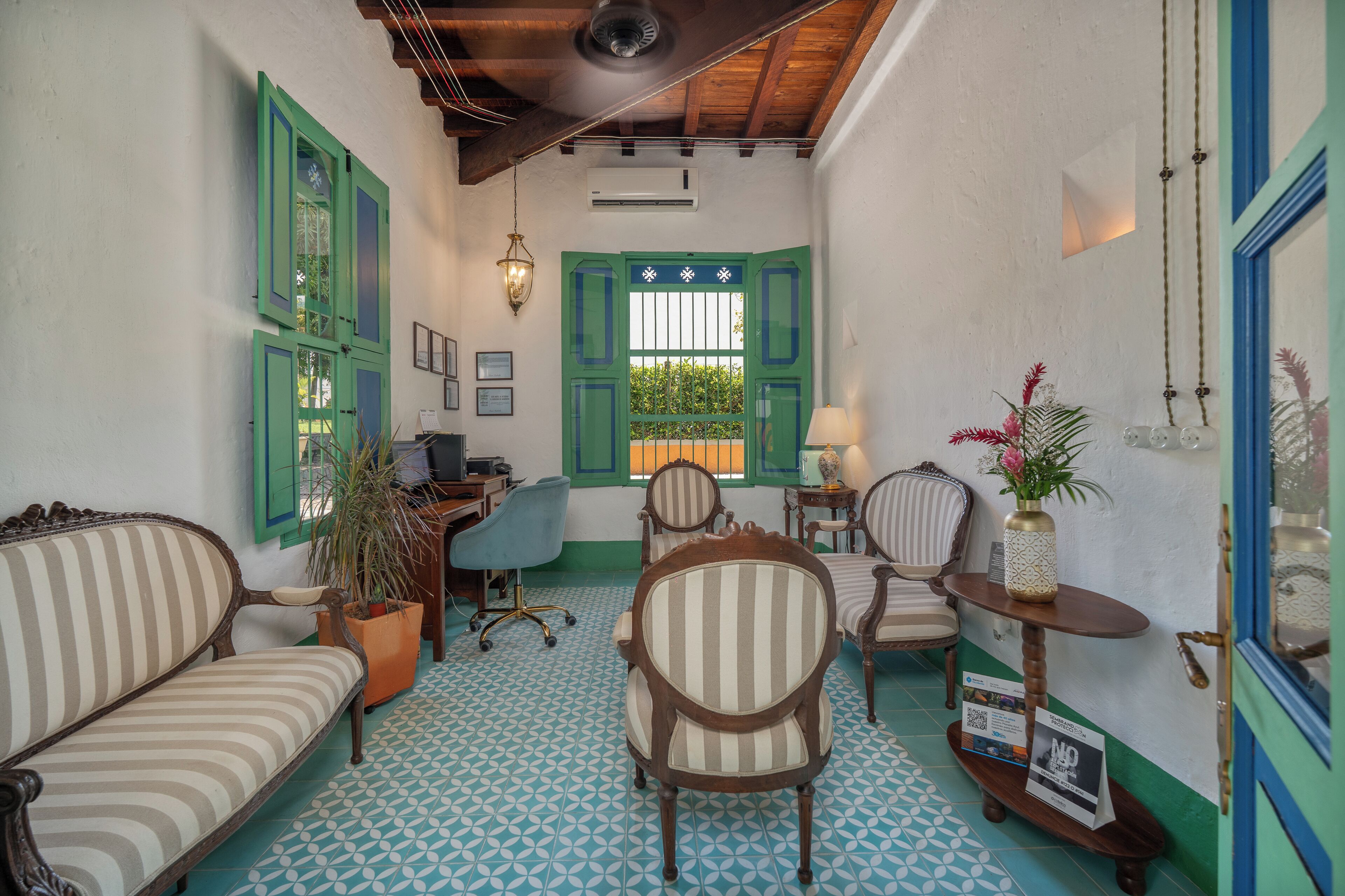 A cozy room with a wooden ceiling, a desk with a chair, a sofa, and a small table with a vase.