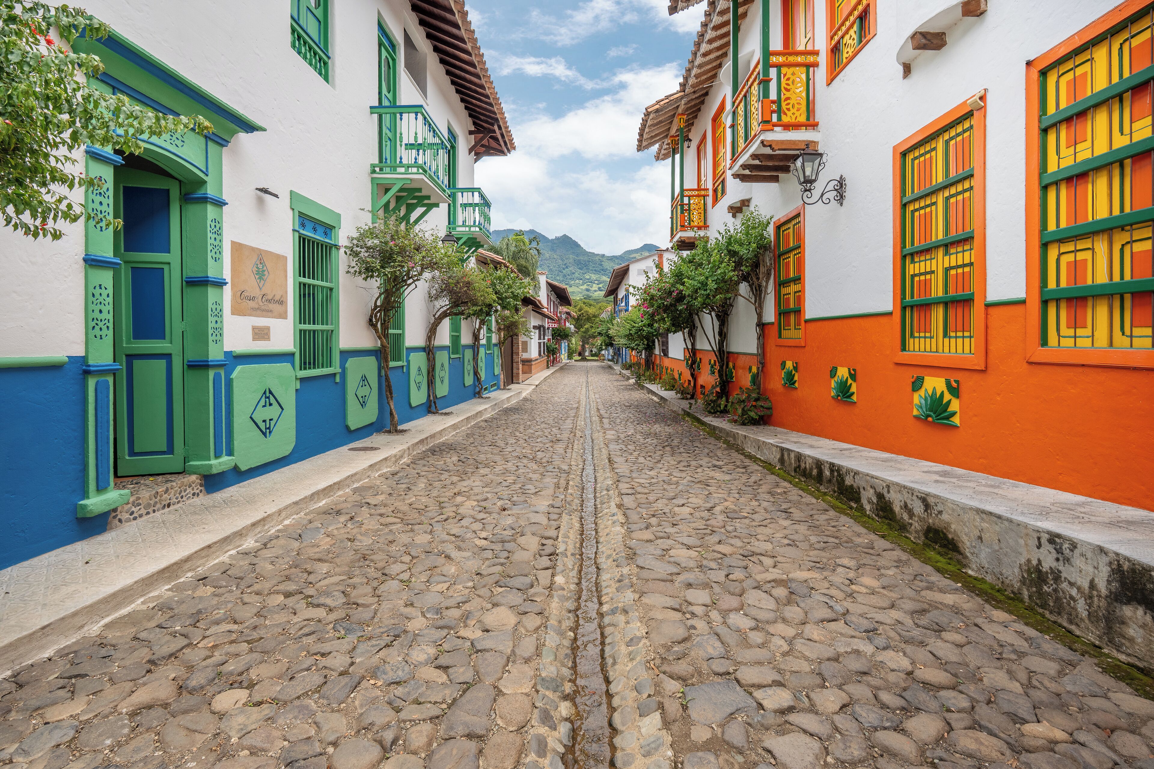 A cobblestone street lined with colorful buildings, a sign reading "Casa Corredor," and a mountain in the background.