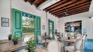 Un comedor con mesas y sillas de madera, plantas en macetas y una cocina al fondo.