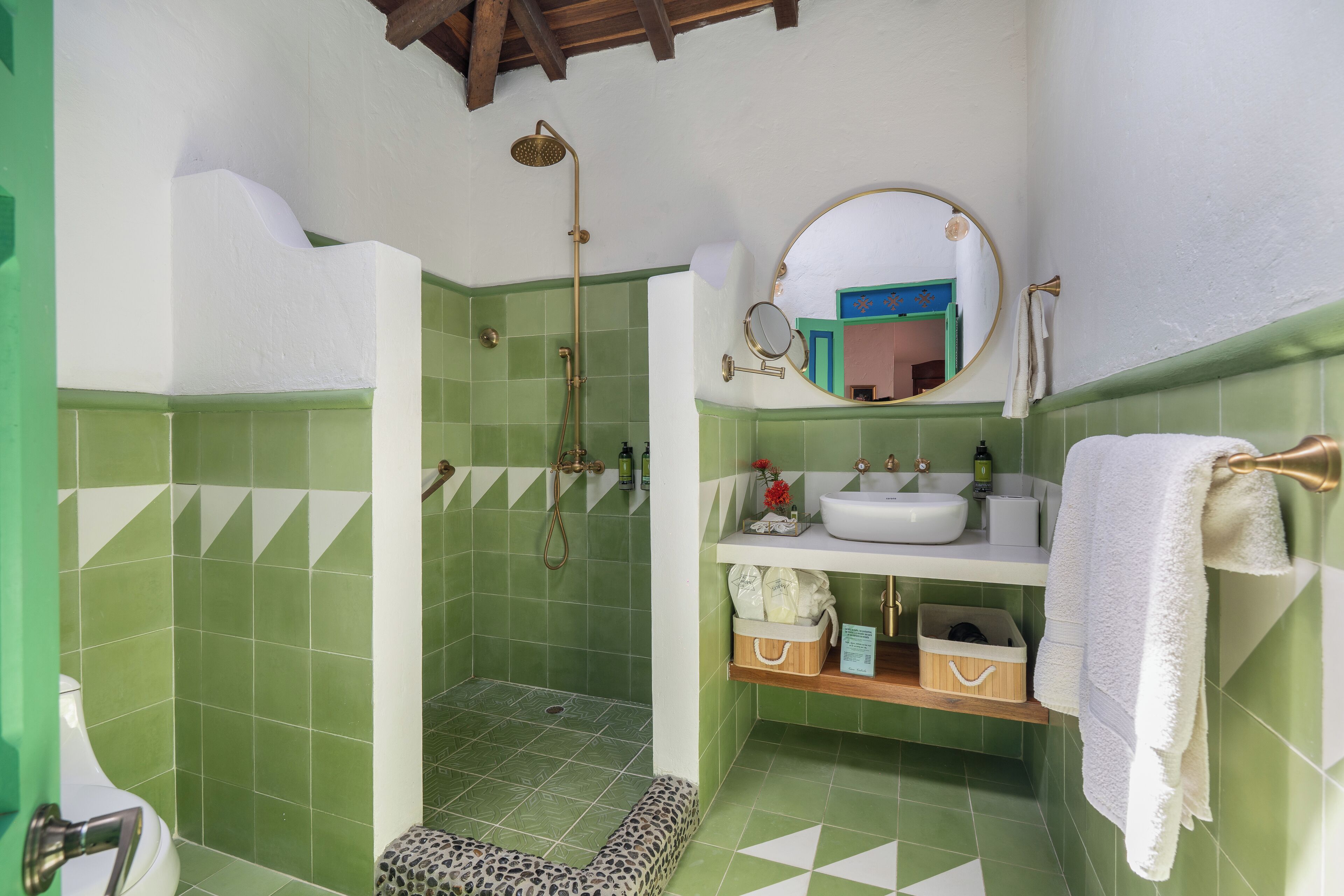 A bathroom with green tiles, a shower, a sink, a mirror, and a towel rack.