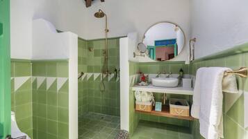 A bathroom with green tiles, a shower, a sink, a mirror, and a towel rack.