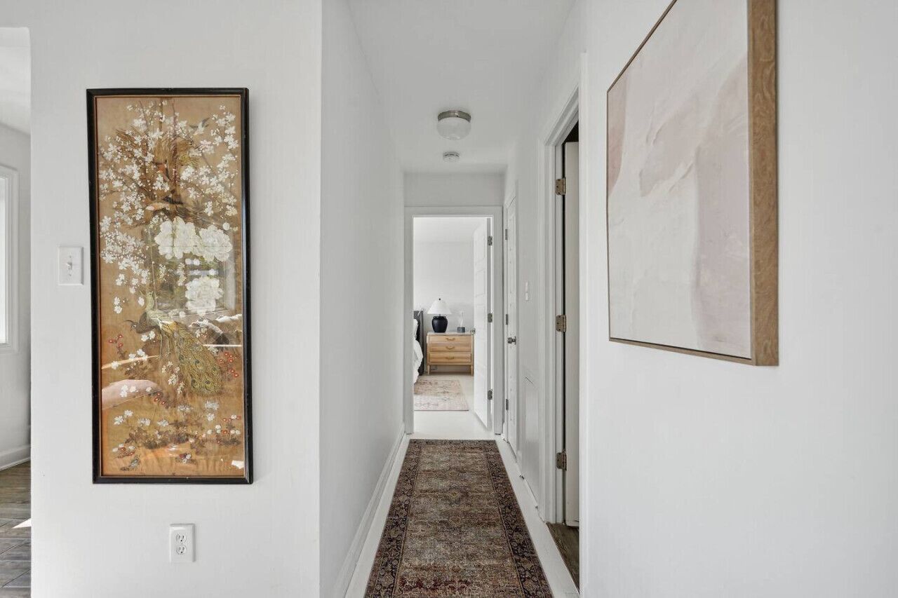A hallway with a patterned rug, a framed painting on the left, and a door on the right.