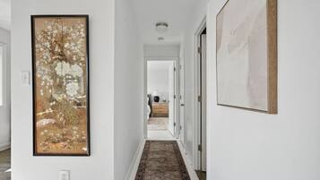 A hallway with a patterned rug, a framed painting on the left, and a door on the right.