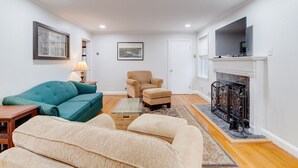 A living room with a sofa, armchair, and ottoman, a fireplace, and a television. - Welcome To Tigertown! 4 Bd House (Towson)