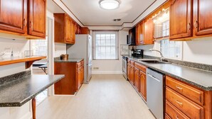 A kitchen with wooden cabinets, granite countertops, a refrigerator, stove, and a window with blinds. - Welcome To Tigertown! 4 Bd House (Towson)