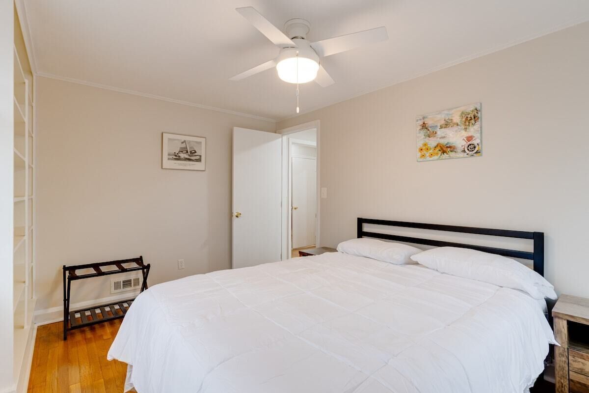A bedroom with a bed, a ceiling fan, a wooden bench, and a door leading to another room.