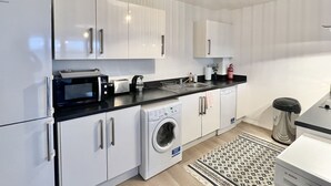 Een moderne keuken met witte kasten, een zwart aanrecht, een magnetron, een broodrooster, een wasmachine en een Bosch koffiezetapparaat.