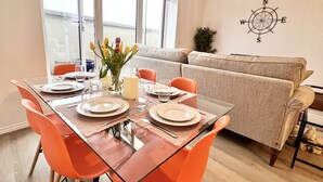 Een eethoek met een glazen tafel, oranje stoelen en een bloemenvaas.