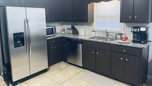 Uma cozinha moderna com armários escuros, eletrodomésticos de aço inoxidável, bancada de granito e uma janela com persianas.