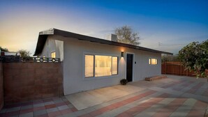 A modern single-story house with a flat roof, a brick wall, and a paved patio with red and grey tiles. - Modern City Ranch Family Home Access by Dirt Road (Palmdale)