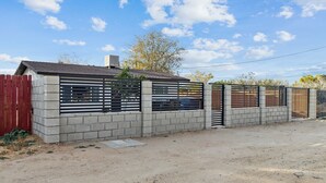 A modern building with a concrete facade, a slatted metal fence, and a red wooden fence. - Modern City Ranch Family Home Access by Dirt Road (Palmdale)