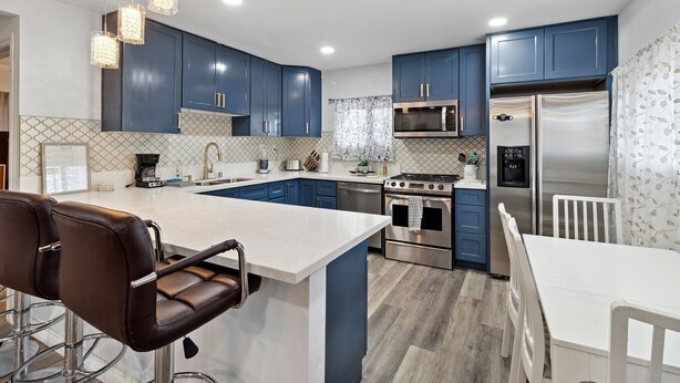 A modern kitchen with blue cabinets, stainless steel appliances, a white island, and bar stools. - Modern City Ranch Family Home Access by Dirt Road (Palmdale)