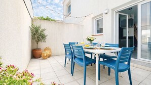 A patio with a table set for four, surrounded by blue chairs, potted plants, and string lights.