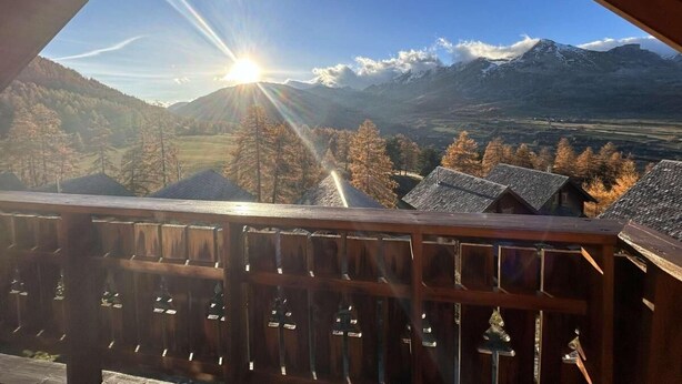 Vista de la montaña desde un balcón de madera, cielo despejado y sol brillante.